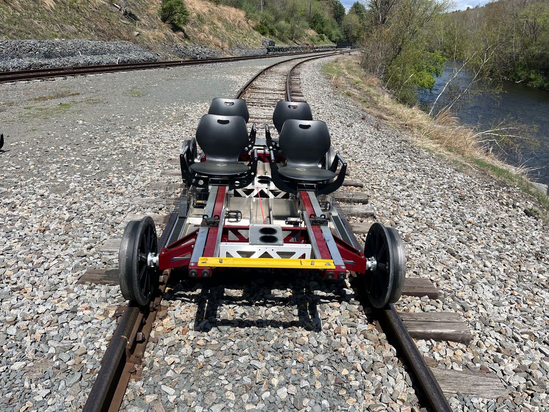Rail Glider on a curving double-track line beside a river, with cup holders and a yellow front bar visible.