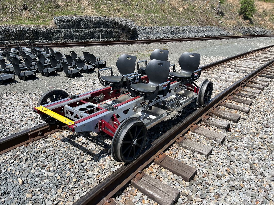 Overhead view of a Rail Glider on the rails, showing adjustable seats, cup holders, a wire basket, and a metal floor under the passengers.