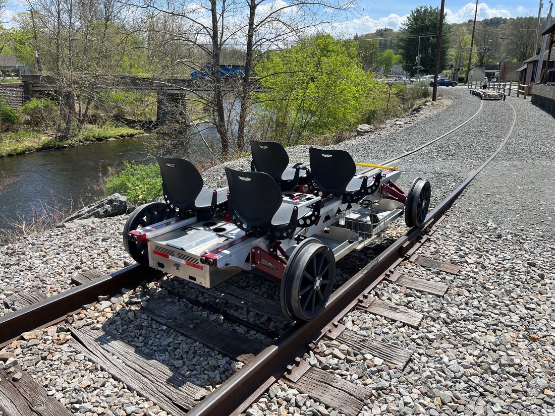 A four-seat Rail Glider on a curved riverside track, with seats reversed so riders can travel the other direction without lifting the bike.